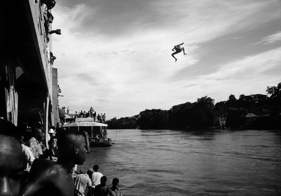 Traders, having boarded a Congo River steamer, the Colonel Kokolo, on its way to Kinshasa from Kisangani, jump off the bridge to join their colleagues for the paddle back upstream to their villages, Congo, (then Zaire), 1996